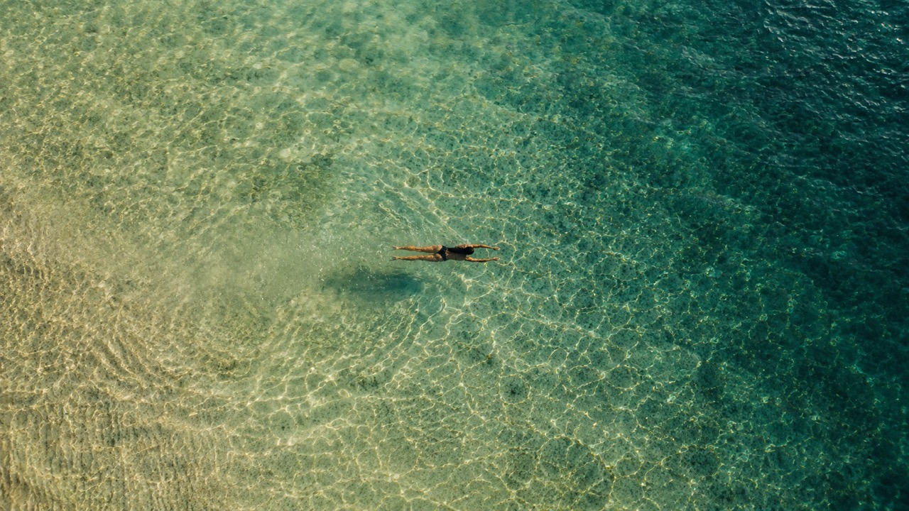 The Silent Blue: Finding Profound Serenity in the World's Most Beautiful Dive Sites 1 - The Socialites Lone Swimmer in Aegean Cove Aerial Large The Socialites